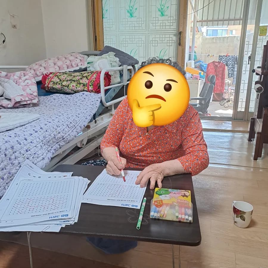 어르신이 탁자에 앉아 색연필로 인지 워크북의 점 잇기 활동을 하시는 모습